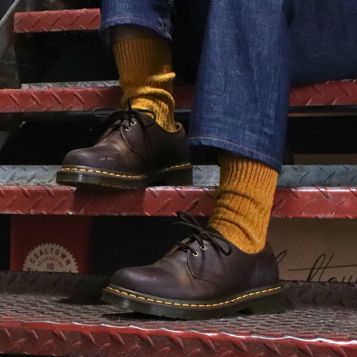 Person wearing brown leather shoes and yellow socks sitting on a set of stairs.