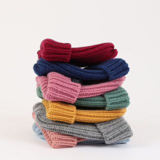 Stack of colourful knitted beanies on a white background