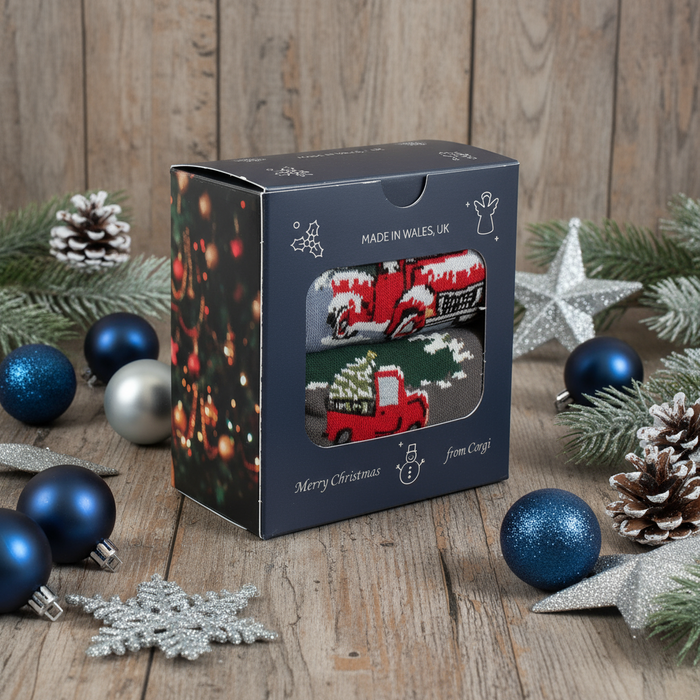 A Men's 2-Pair Christmas Truck Gift Box with a Christmas tree and truck design, placed near a golden Christmas ornament on a grey surface.