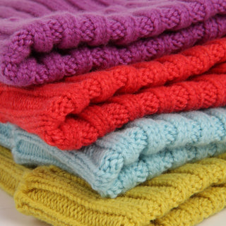 Stack of folded knitted blankets in purple, red, blue, and yellow.