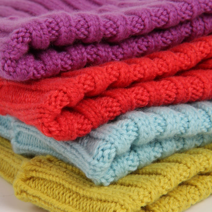 Stack of folded knitted blankets in purple, red, blue, and yellow.