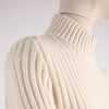 Close-up of a white ribbed sweater on a mannequin against a light background showing the shoulder detail