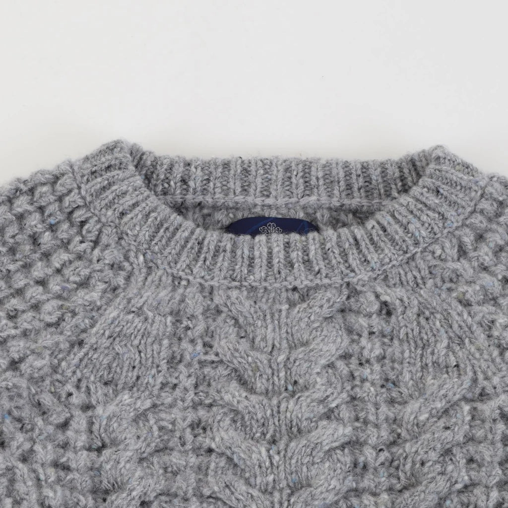 Close-up of a gray cable-knit sweater showing the textured knit pattern and a small dark blue neck label.