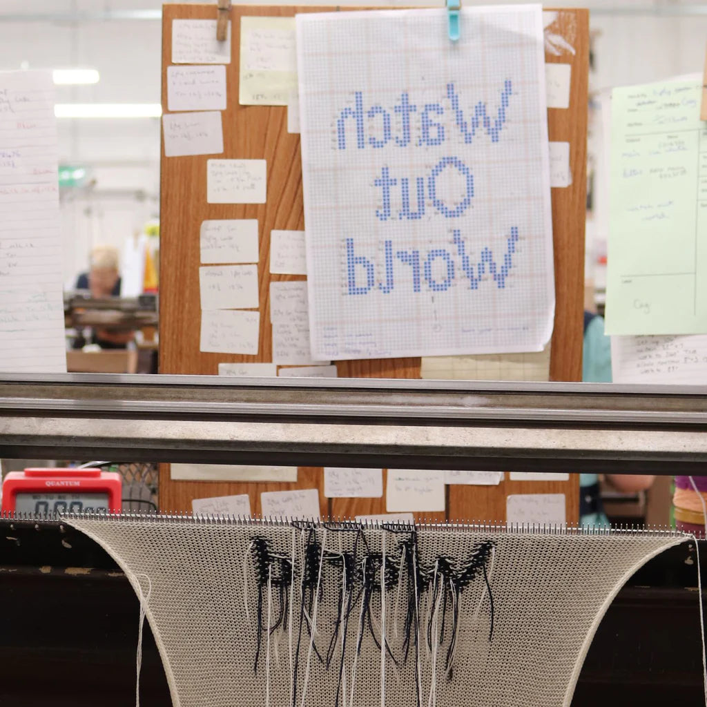 knitted fabric with 'watch out world' knitting on a loom in a workshop setting
