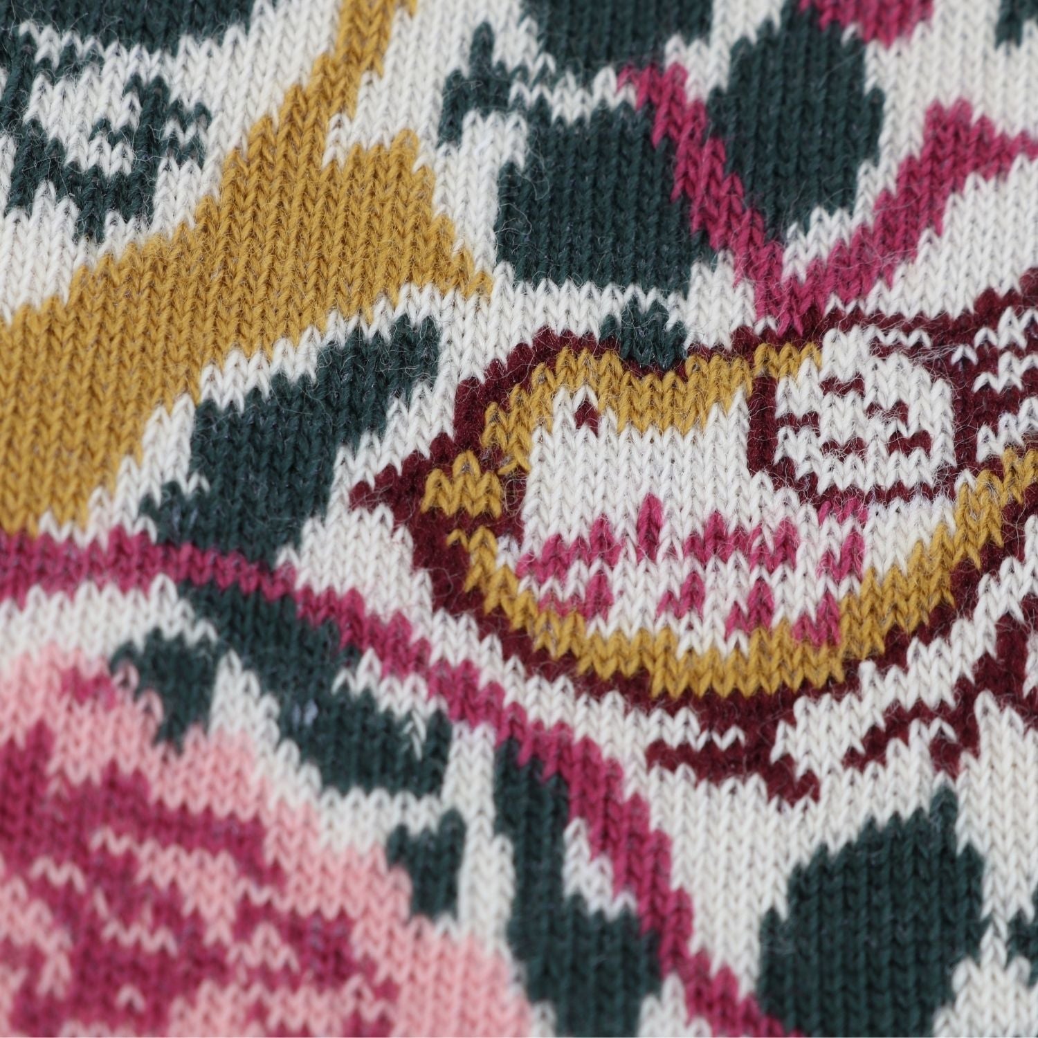 Close-up of a knitted textile with a multicolor pattern featuring white, dark green, pink, and mustard yellow.