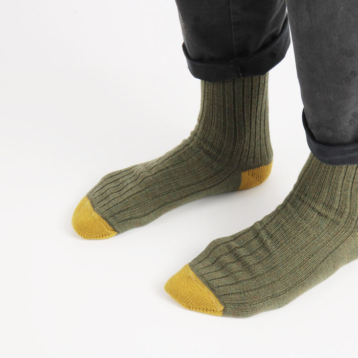 Green socks with yellow toes and cuffs worn by a person on a white background