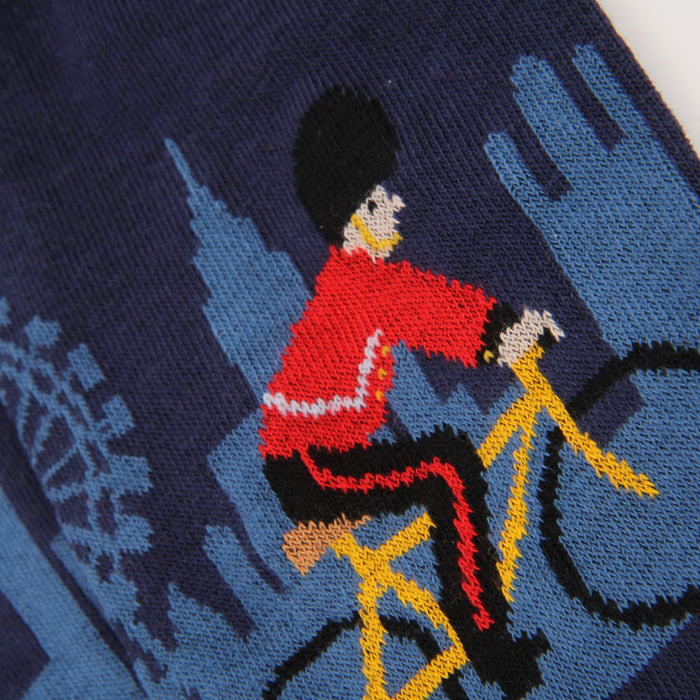 Knitted design of a Royal Welsh Guard on a bicycle with a London landscape background