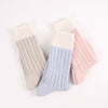 Three pairs of knitted socks in beige, light blue, and pink on a white background