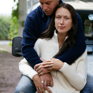 A woman wearing a white ribbed zip cashmere cardigan with a stand-up collar, long sleeves, and ribbed cuffs. She is sitting and holding hands with a man who is partially visible.