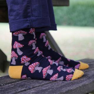 Navy socks with red mushroom pattern and yellow accents worn outside on a bench