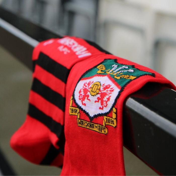Red sports socks with black stripes and red socks with Wrexham crest logo on a metal railing.
