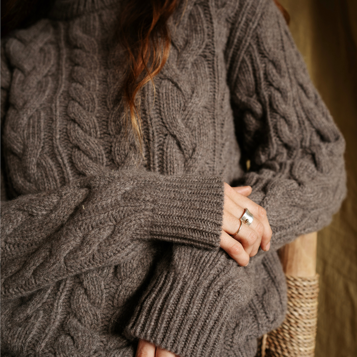 Close-up of a person wearing a cable knit sweater with a blurred background