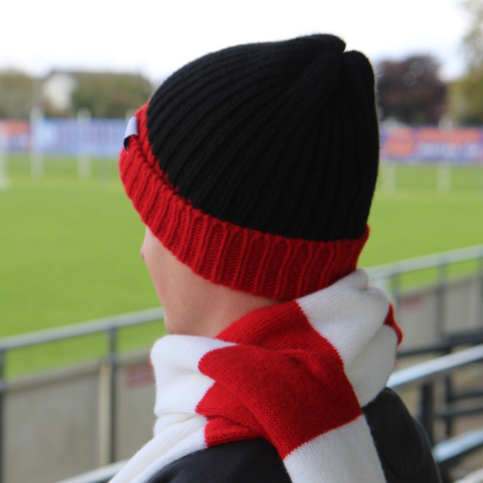 Person wearing a black and red knit hat with a matching scarf in a stadium setting