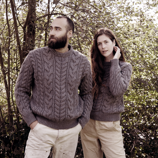 Two people wearing matching cable knit sweaters standing in a forest.