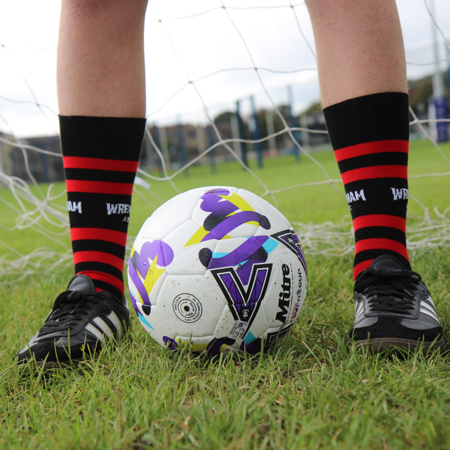 Person wearing black and red striped socks with a soccer ball on a grass field.