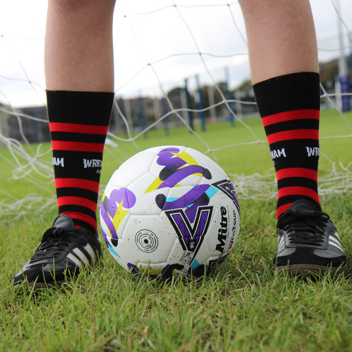 Person wearing black and red striped socks with a soccer ball on a grass field.