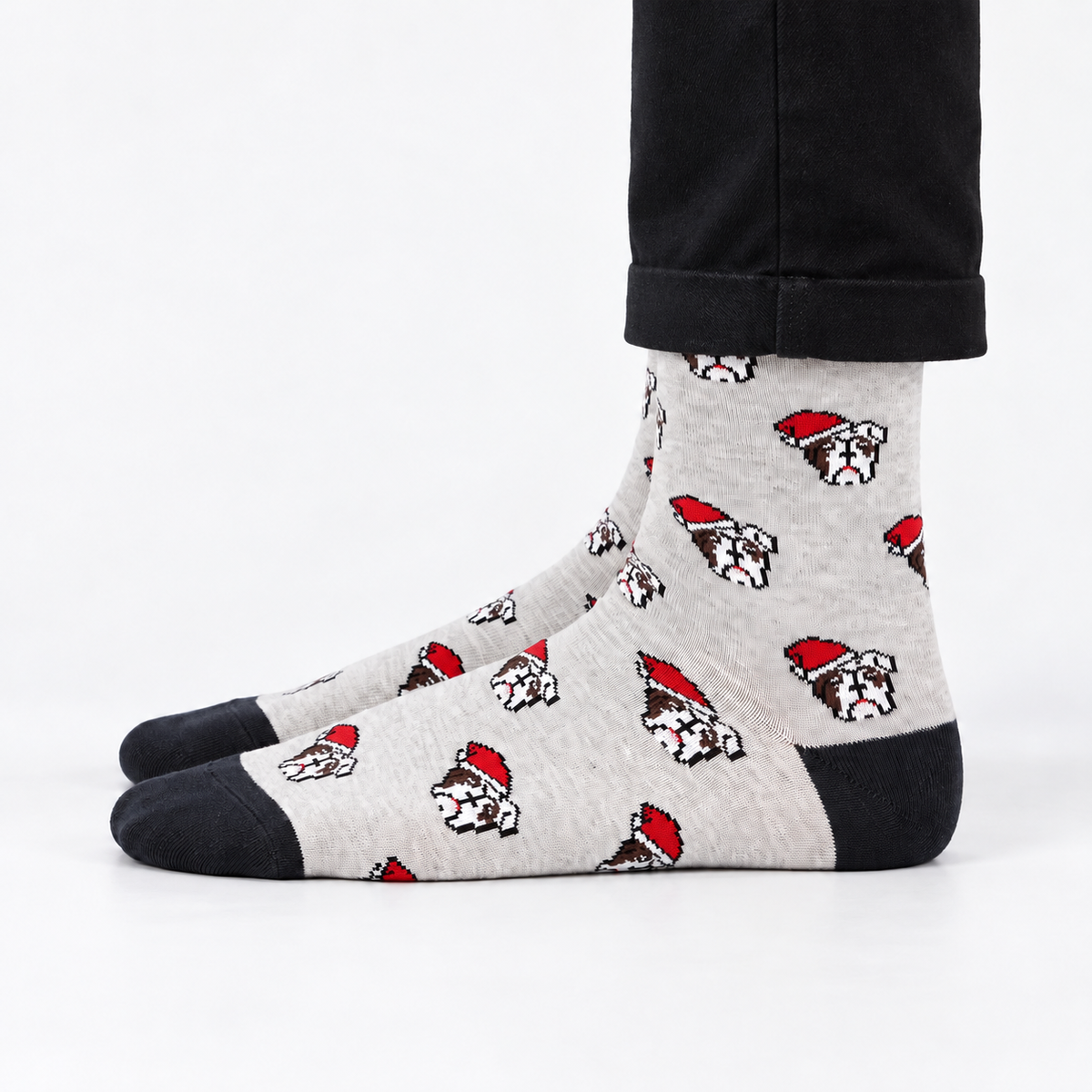 A pair of crew socks with a light gray heather background, featuring a repeating pattern of bulldog faces wearing red Santa hats, with black toes, heels, and cuffs. The socks are modeled with black pants against a clean white background.
