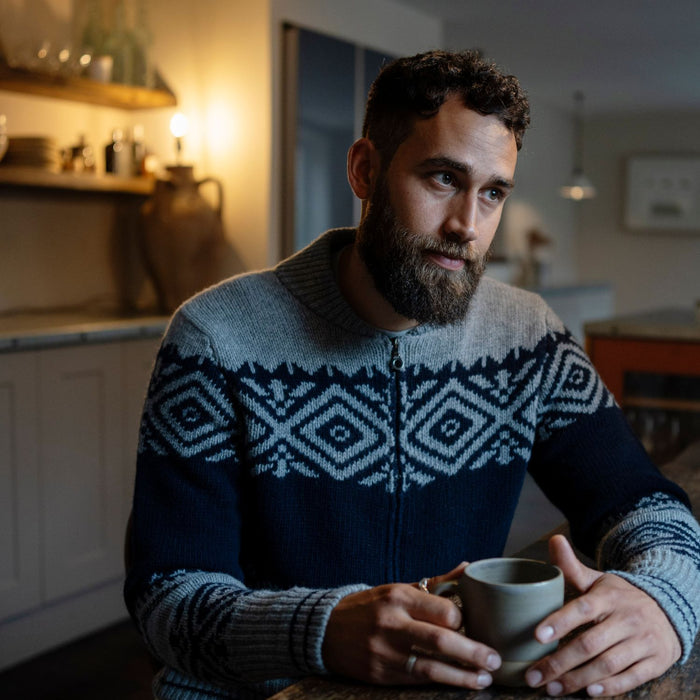 Man in a patterned sweater holding a mug in a kitchen.