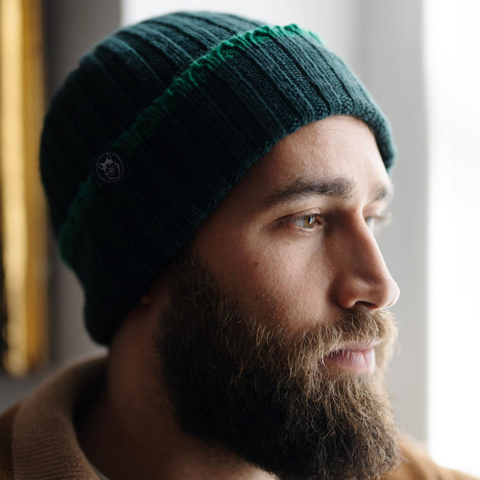 A man wearing a green cashmere beanie with contrasting green tips, looking contemplative.