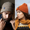 Two models wearing ribbed knit beanie hats. One hat is beige and the other is orange, both with a tweed fleck throughout and a folded brim.