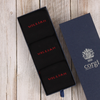Navy socks with 'WILLIAM' embroidery in red text, inside an open navy box with 'Corgi' branding.
