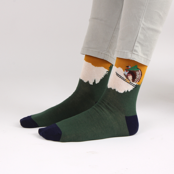 Green and mustard yellow sock with a turkey on a pair of skis, socks photographed on a white background