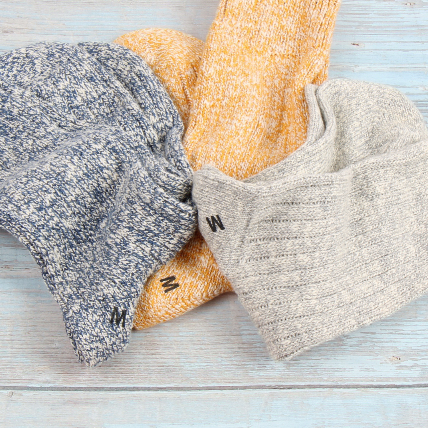 Three pairs of socks in gray, yellow, and beige on a light wooden surface.