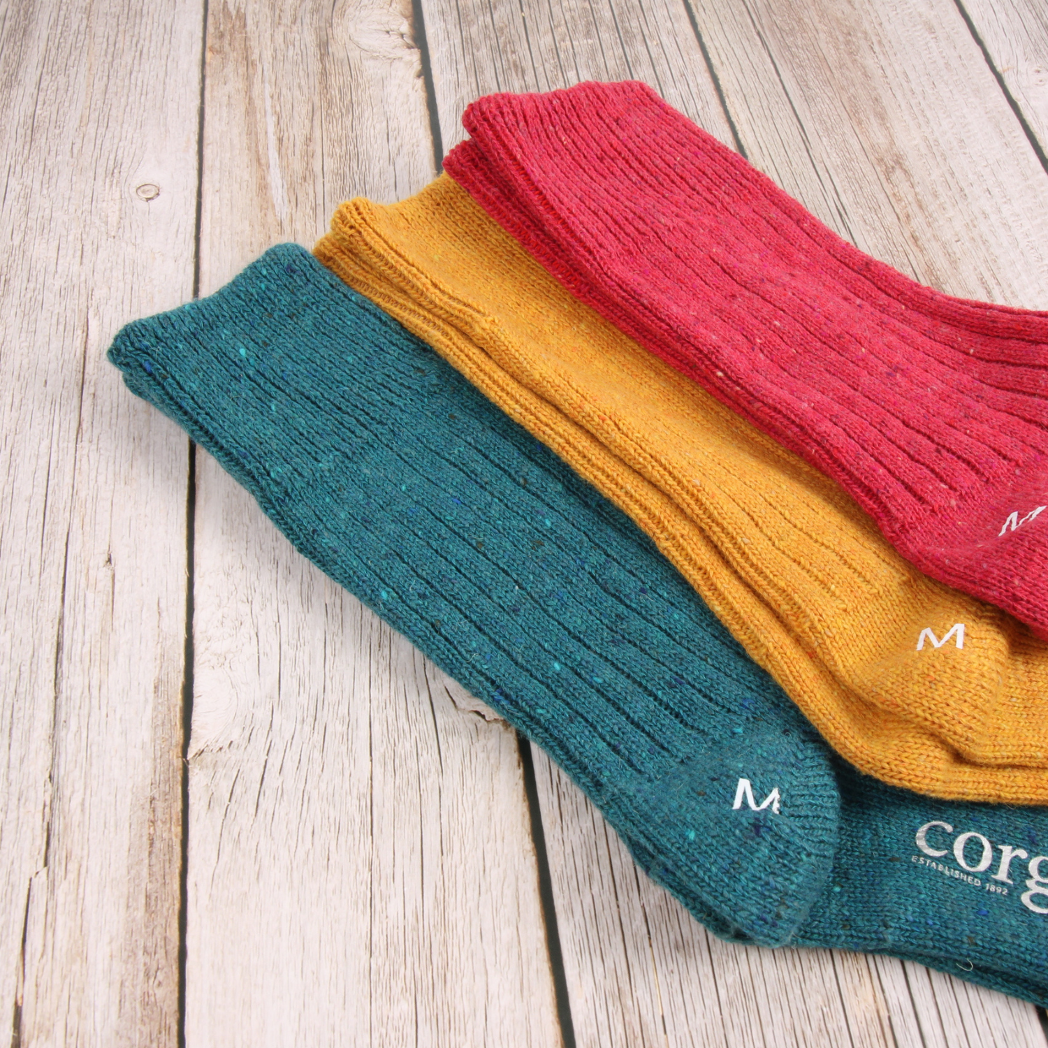 Three pairs of colorful socks stacked on a wooden surface, with 'Corgi' branding visible.