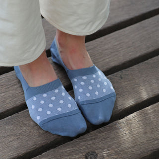 A pair of blue invisible socks with a white polka dot pattern, displayed on a person's feet, showing the socks' subtle design above the shoe line.