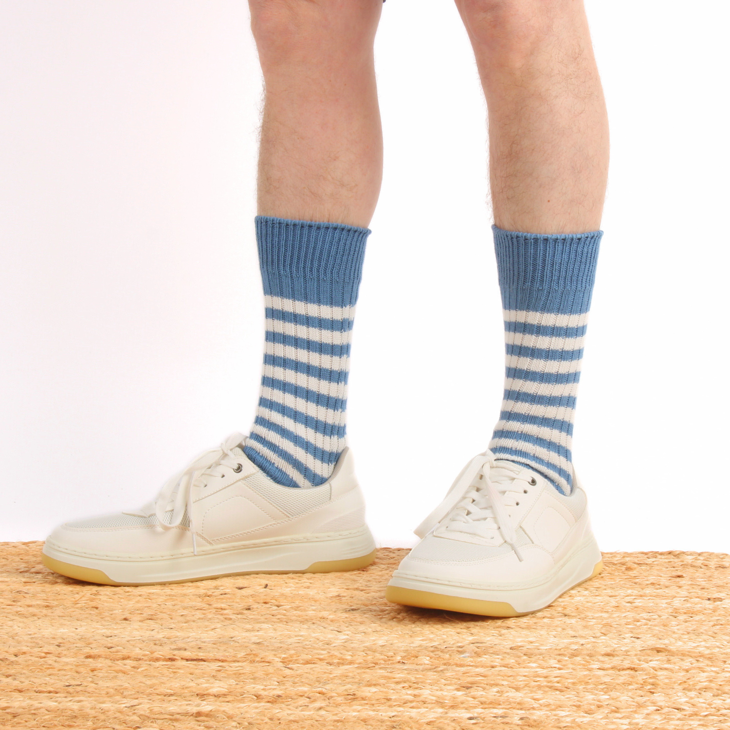 Blue and white striped socks worn with white sneakers on a neutral background