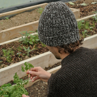 Person wearing a knit hat and sweater tending to plants in a garden.