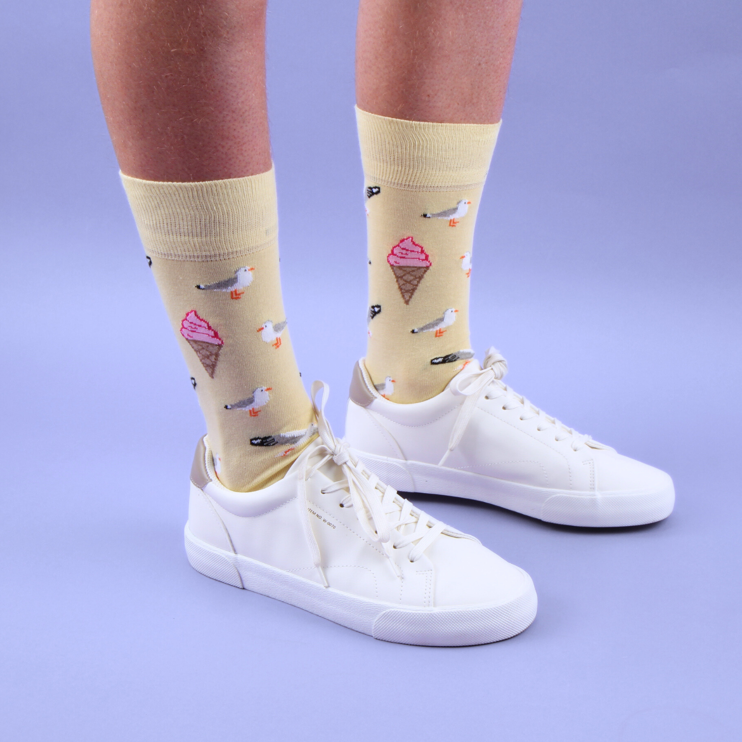 Pale yellow socks with ice cream and bird pattern worn with white sneakers on a purple background