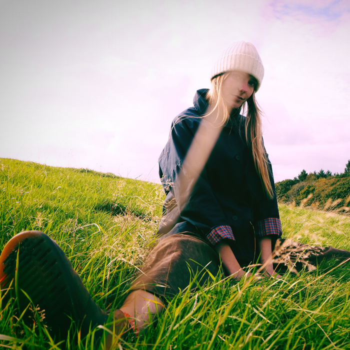 Person sitting on a grassy hill with a scenic background wearing a cream hat