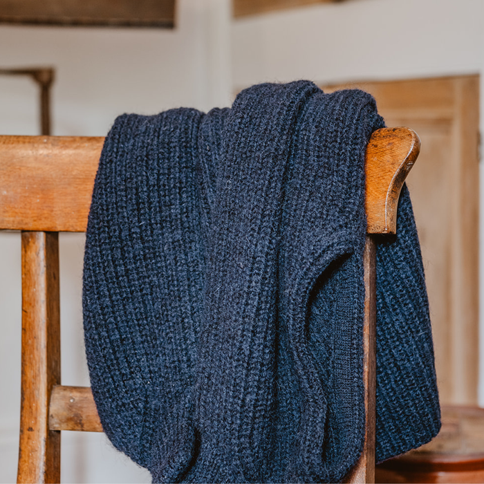 Blue knitted sweater draped over a wooden chair indoors