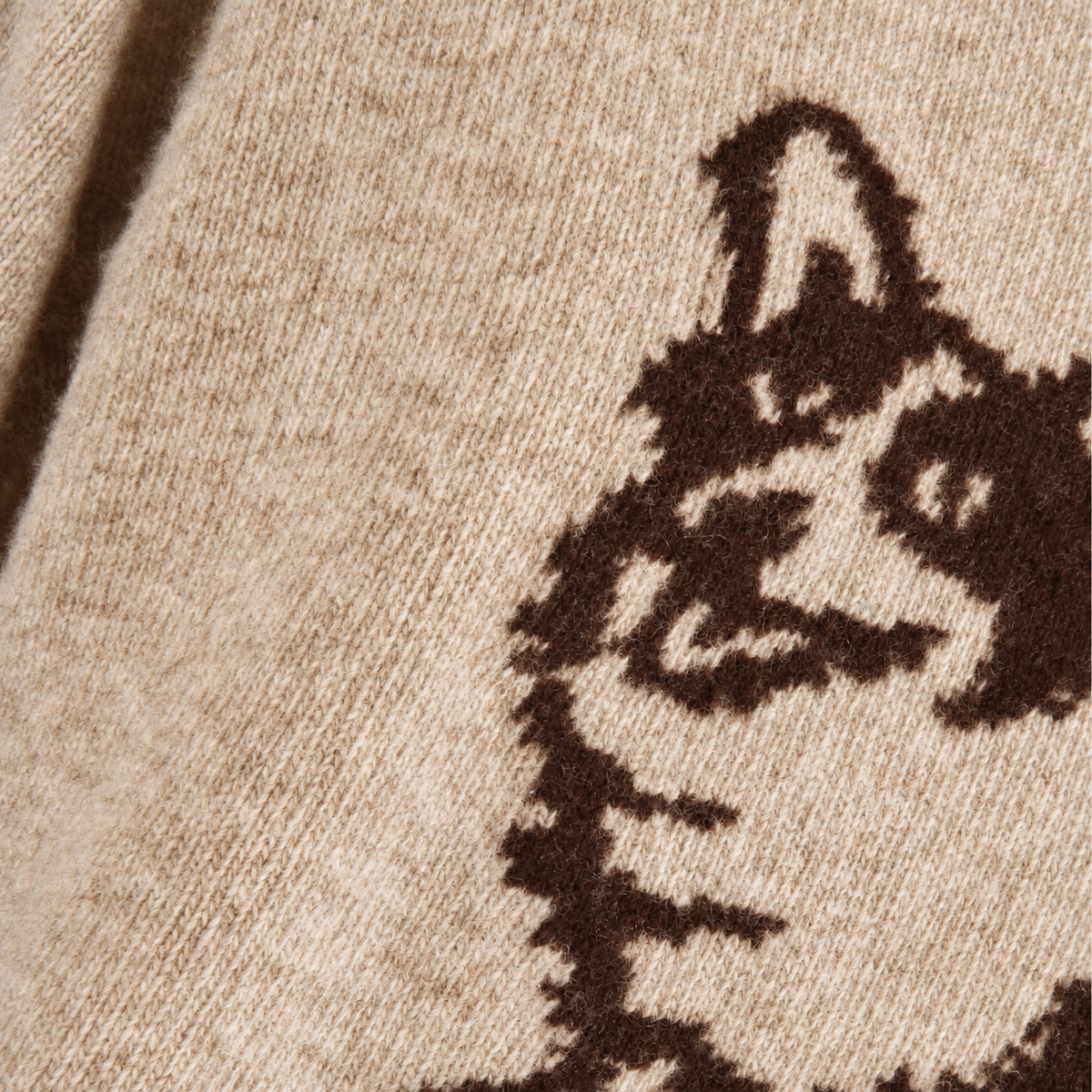 Close-up of a beige knit fabric with a dark brown graphic pattern, showing the texture of the yarn and part of the design.
