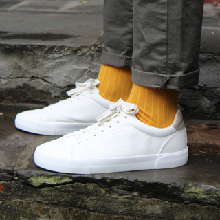 White sneakers worn with yellow socks on a stone surface