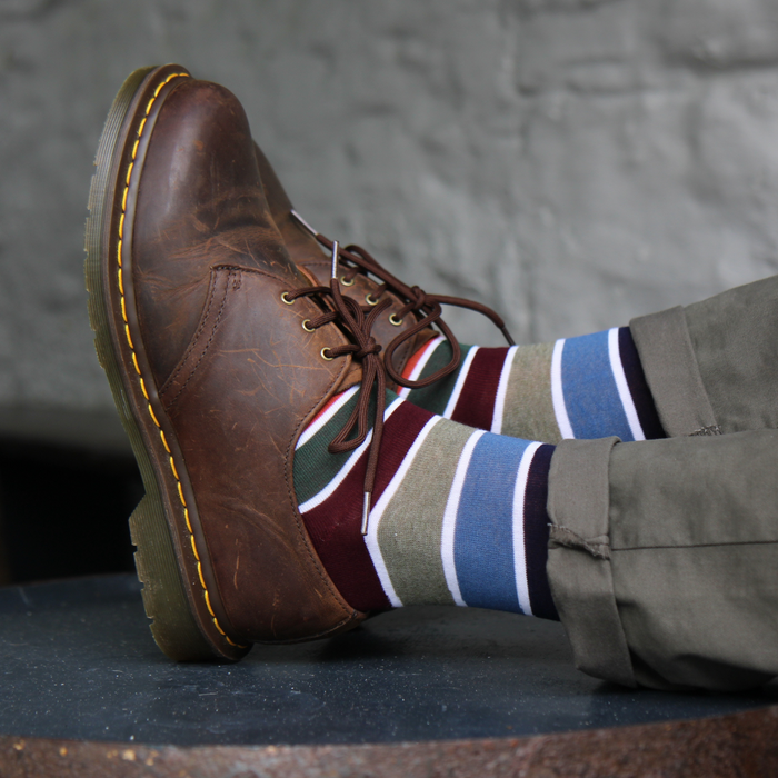 Brown leather shoe with a striped sock on a gray background