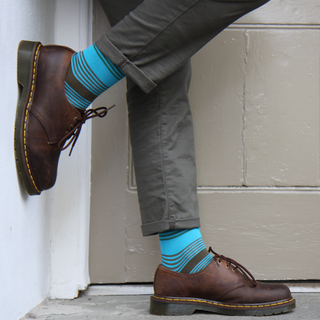 Person wearing brown shoes and blue striped socks against a neutral wall.