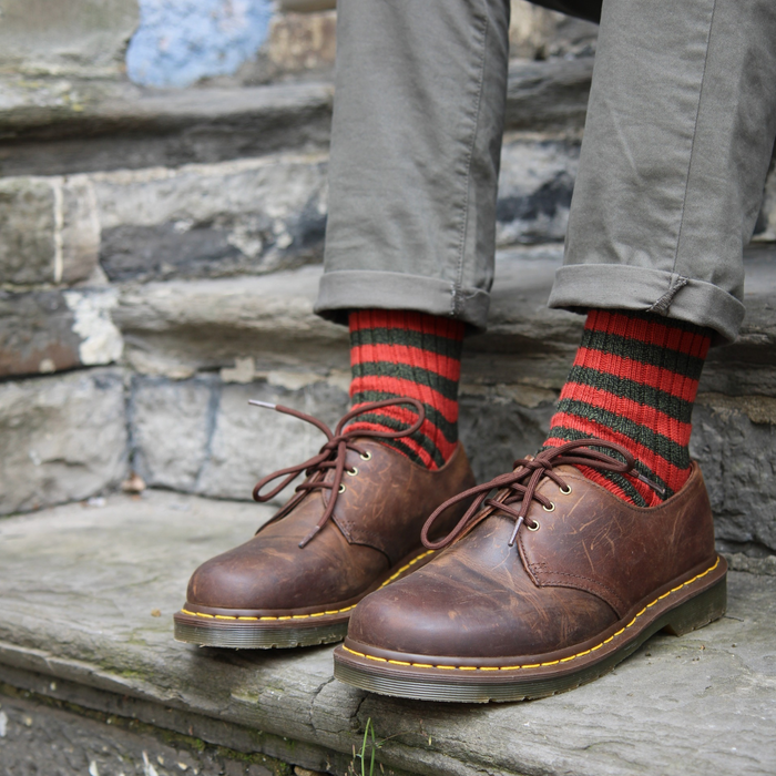 Brown leather shoes with orange and green striped socks on a stone step.