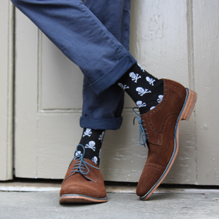 Person wearing brown shoes and black socks with skull patterns against a neutral background