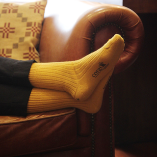 Person wearing yellow boot socks with a brand logo, sitting on a brown leather chair.