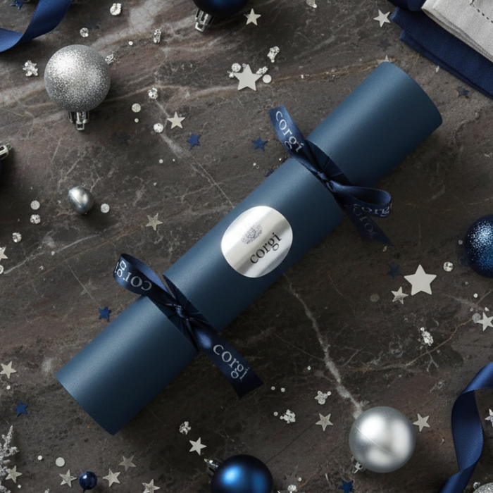 Blue Christmas cracker with 'Corgi' branding on a dark surface with festive decorations.
