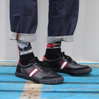 A pair of men's socks featuring a pattern with a red double-decker bus and the London Eye, worn on the lower leg area visible above rolled-up blue jeans.