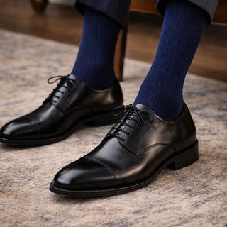 Black dress shoes with blue socks on a textured surface