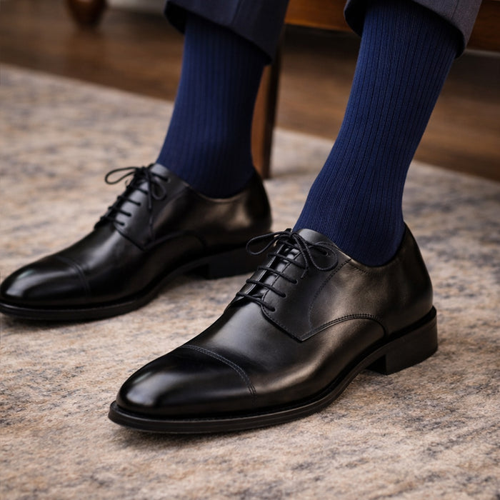 Black dress shoes with blue socks on a textured surface