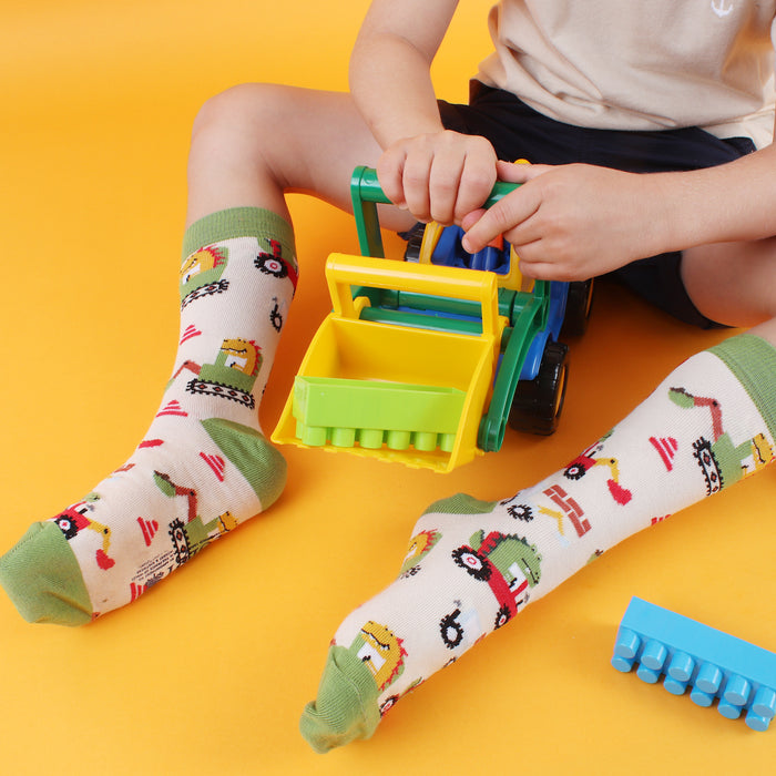 A child wearing green and white patterned socks with dinosaur and digger designs, sitting next to toy vehicles.