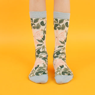 A pair of kids' socks with a William Morris Honeysuckle floral pattern in cream and pink colors, with a pale blue cuff, heel, and toe.