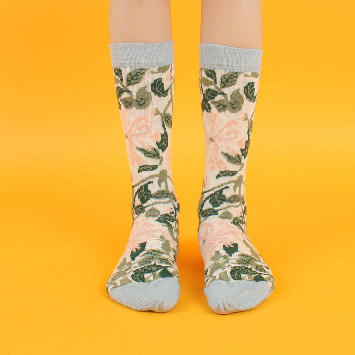 A pair of kids' socks with a William Morris Honeysuckle floral pattern in cream and pink colors, with a pale blue cuff, heel, and toe.