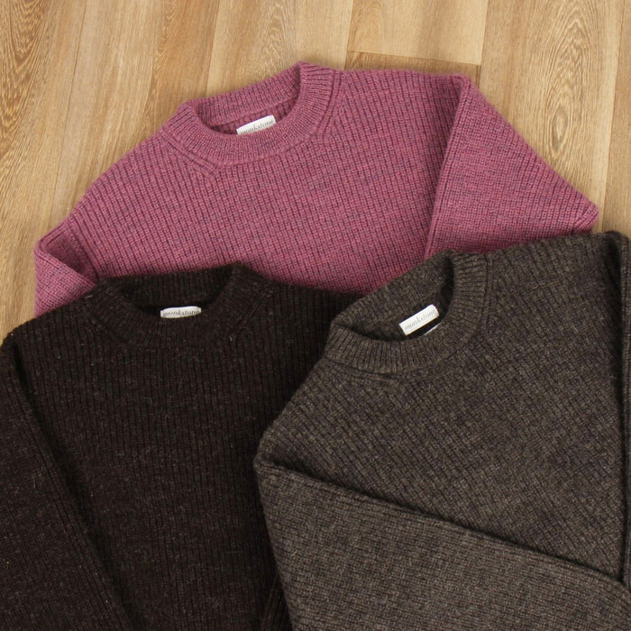 Three folded sweaters in purple, brown, and gray on a wooden surface