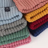 Stack of colourful knitted beanie hats with a brand tag on a white background